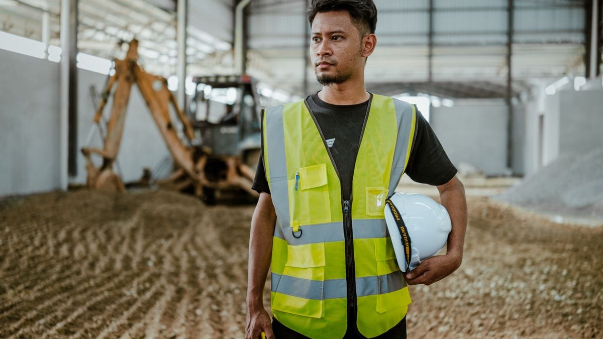 Site supervisor in a safety vest holding a hard hat at a construction site