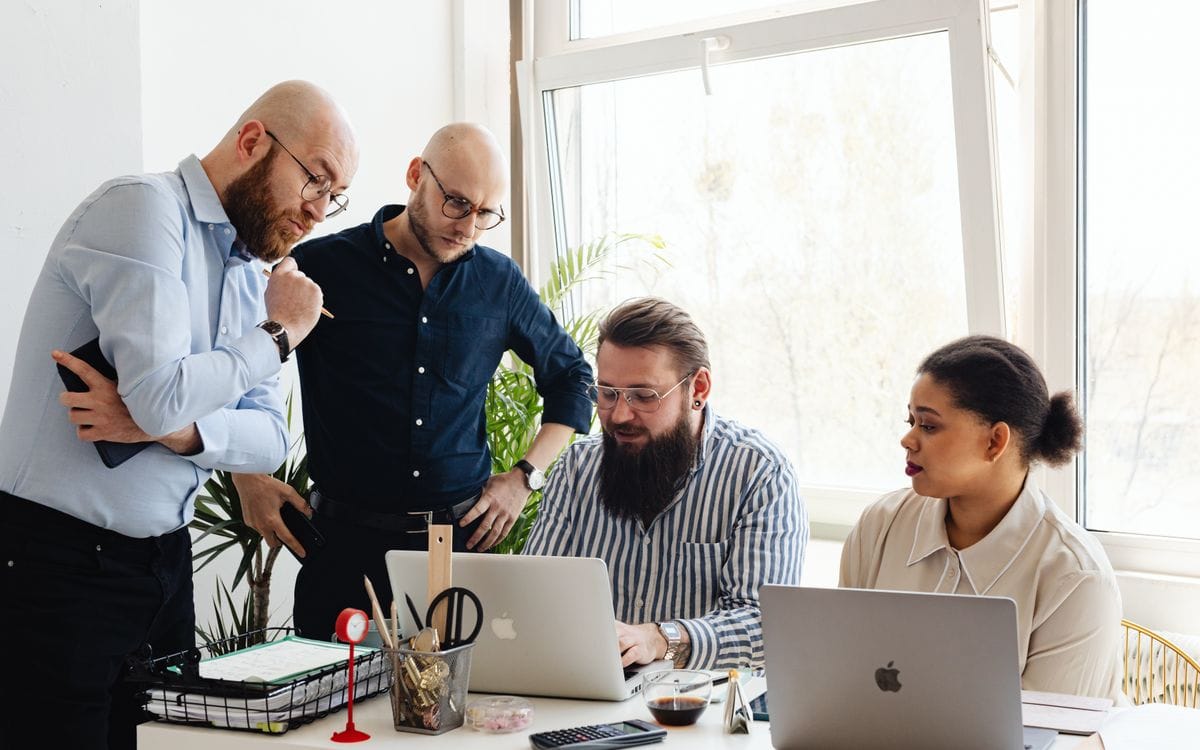 Team gathered around two laptops reviewing work at an office desk